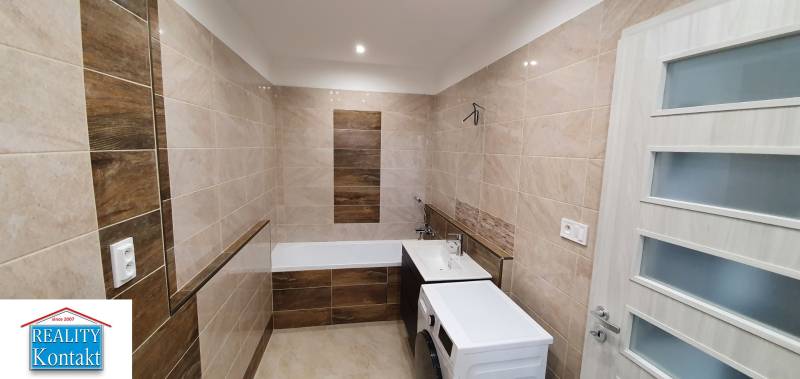 Bathroom with a bathtub and a washing machine in a 2-room apartment, tiles with a wooden decor.