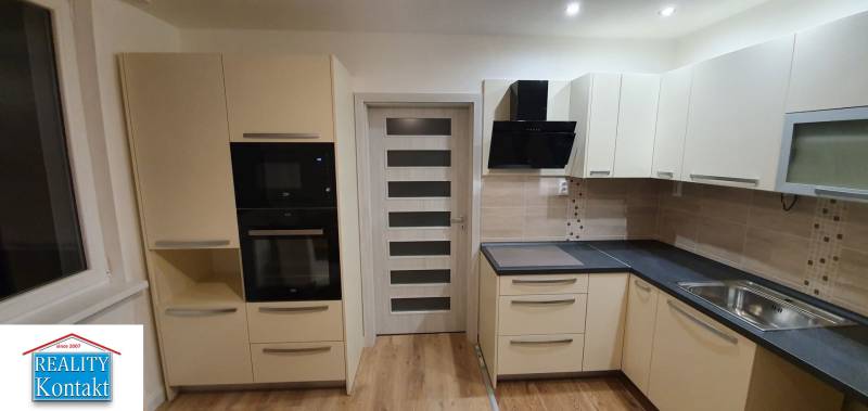 A kitchen in a 2-room apartment with modern cabinets, appliances, and a wooden decor floor.
