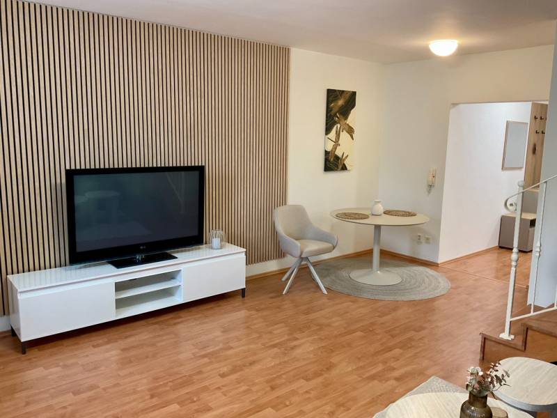 Living room in a 3-room apartment with a TV, armchair, table, and floor with a wooden decor.
