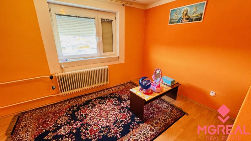 A room in a family house with an orange wall, carpet, radiator, and table.