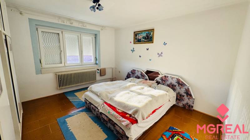 A bedroom in a family house with a carpet and a window with a blind.