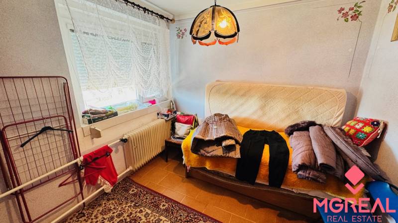 A room in a family house with a sofa, clothes, a carpet, and a lamp.