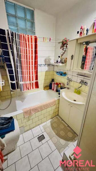 A bathroom in a family house with a bathtub, a sink, shelves, and colorful towels.