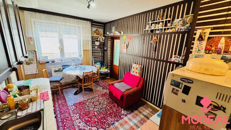 A kitchen in a family house with a living room, an armchair, a carpet, a dining table, and decorations.
