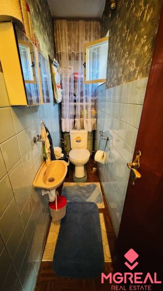 A narrow bathroom in a family house with blue tiles and a floor with a wooden decor.