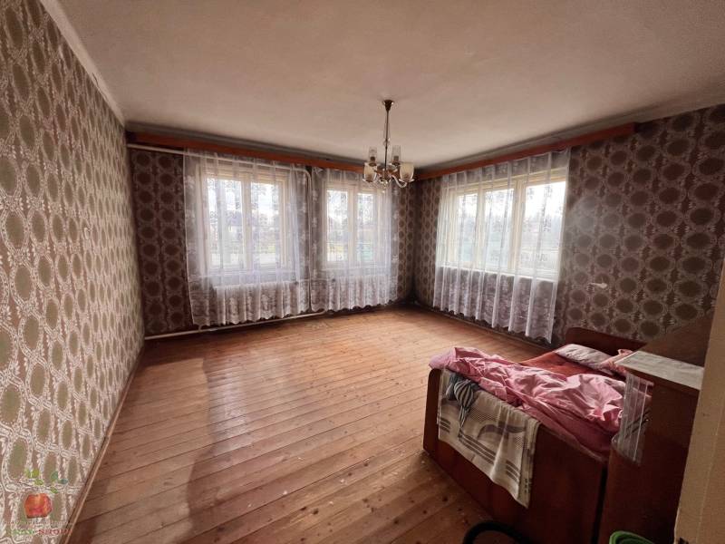 A room in a family house with a wooden decor floor, wallpapered walls, and a chandelier.