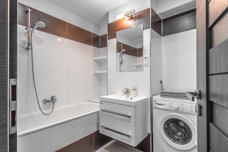 Bathroom in a 3-room apartment with a bathtub, sink, mirror, and washing machine.