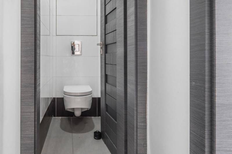 A simple toilet in a 3-room apartment with white tiles and gray doors.