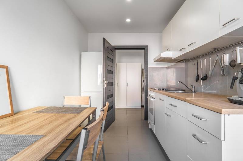 Kitchen in a 3-room apartment with white cabinets, wooden table, and storage space.