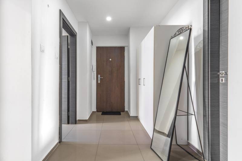 A hallway in a 3-room apartment with tiles, a standing mirror, and white cabinets.