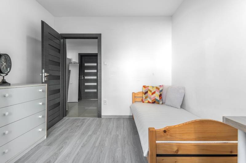 A room in a 3-room apartment with a bed, a dresser, and a floor with a wood decor.