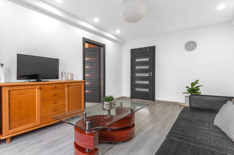 Living room in a 3-room apartment with a sofa, television, and a wooden decor floor.