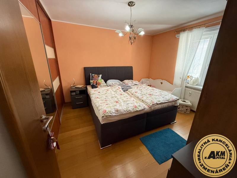 Bedroom in a two-room apartment with a double bed, orange walls, and wood-patterned flooring.