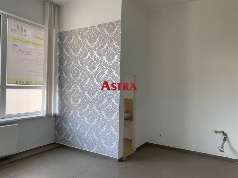 Interior of an office with a window, radiator, and tiled floor, patterned wallpaper on the wall.