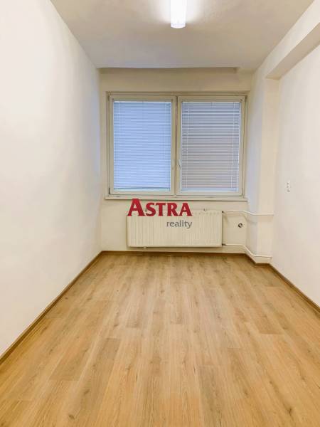 An office with a wood-patterned floor, white walls, a window with blinds.
