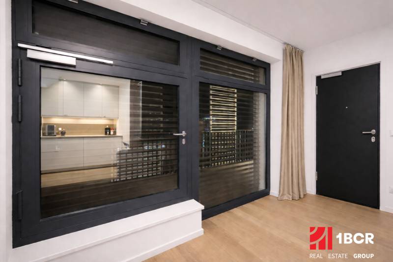 1-bedroom apartment with wood-patterned flooring, large window, and curtains.