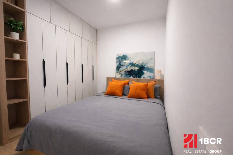 A bedroom in a studio apartment with a wardrobe, art on the wall, and orange pillows.
