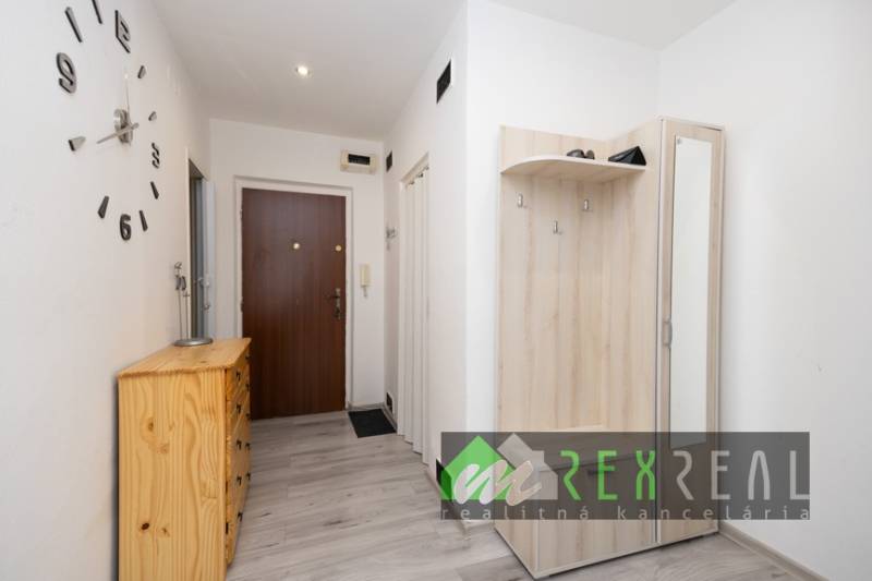 A hallway of a 3-room apartment with a coat rack, furniture, and flooring with a wooden decor.