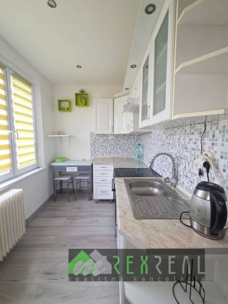 A kitchen in a 3-room apartment with a wood-patterned floor and light cabinets.