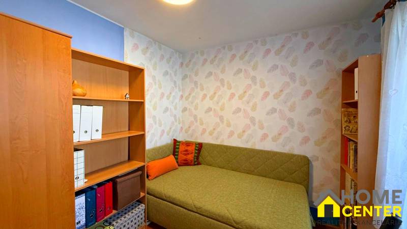 Room in a 3-room apartment with colored walls, a couch, and shelves with books.