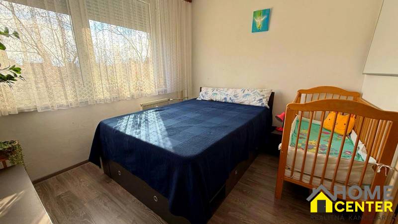 Bedroom in a 3-room apartment with a double bed, a baby crib, and a floor with a wooden decor.