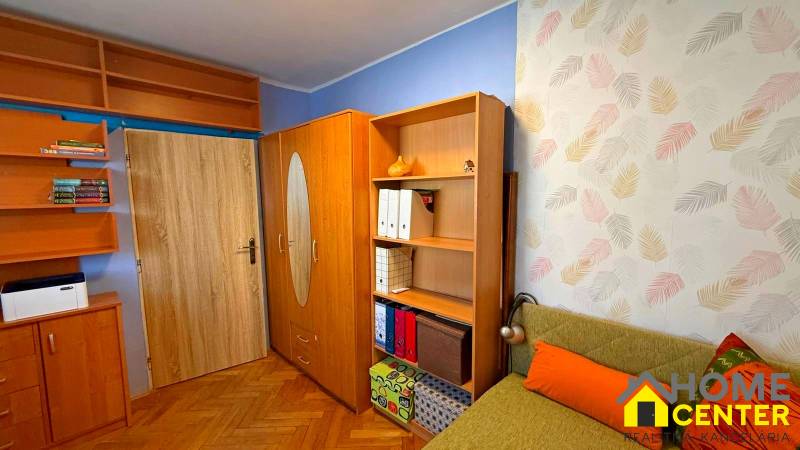 A room in a 3-room apartment with a wood-patterned floor and colorful wallpaper.