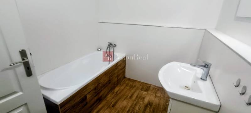 A bathroom in a family house with a bathtub, a sink, and a floor with a wooden decor.