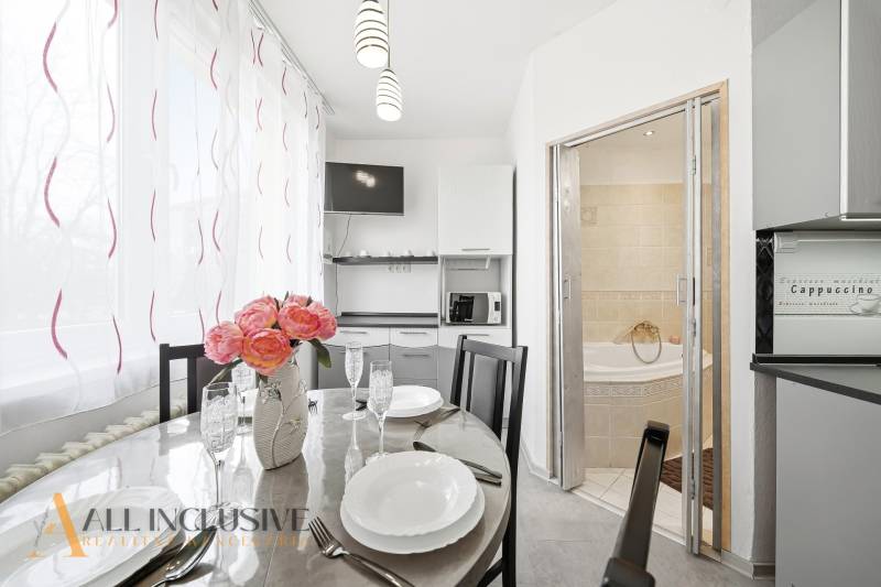 A dining room with flowers and a kitchen in a 3-room apartment, next to a bathroom with a corner bathtub.