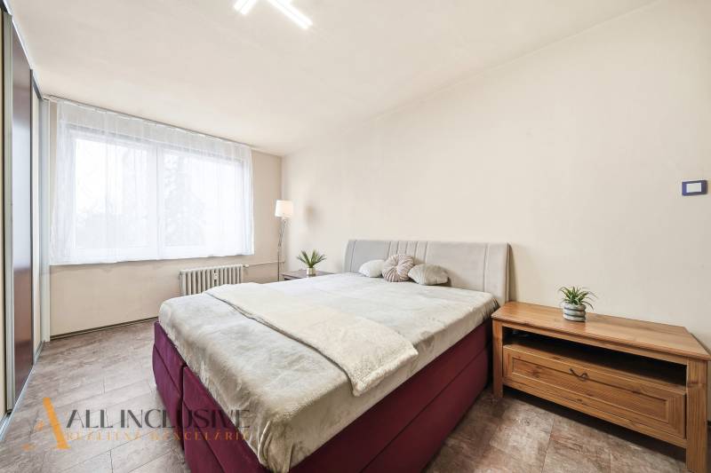 Bedroom in a 3-room apartment with a comfortable bed, dresser, and wooden decor flooring.