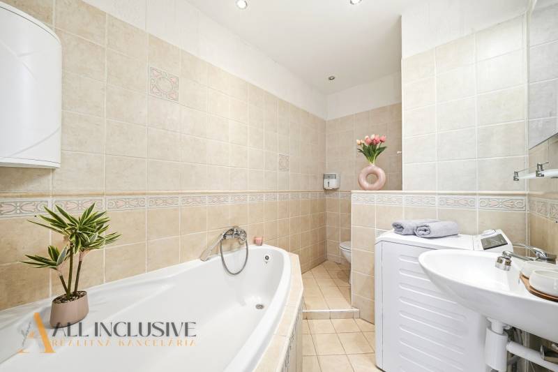 Bathroom in a 3-room apartment with a bathtub, sink, washing machine, and a decorative plant.
