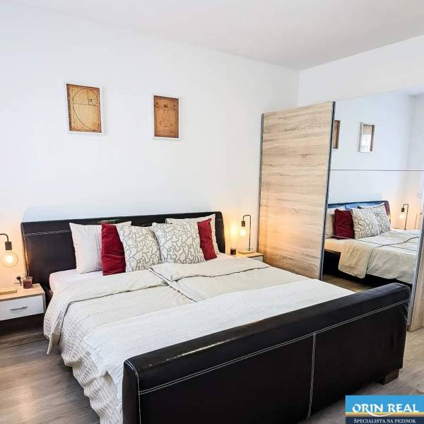 Bedroom in a 2-room apartment with a wood-patterned floor and a large mirror.
