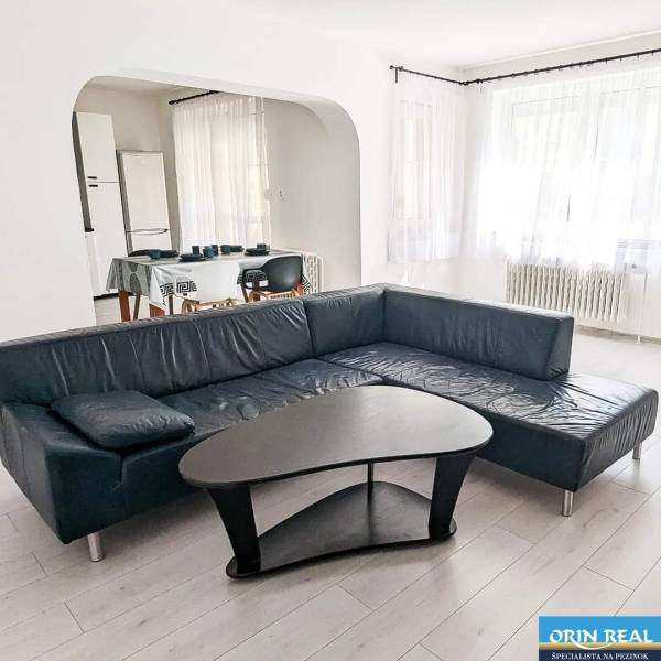 Living room in a two-room apartment with a leather sofa, a table, and a wooden decor floor.