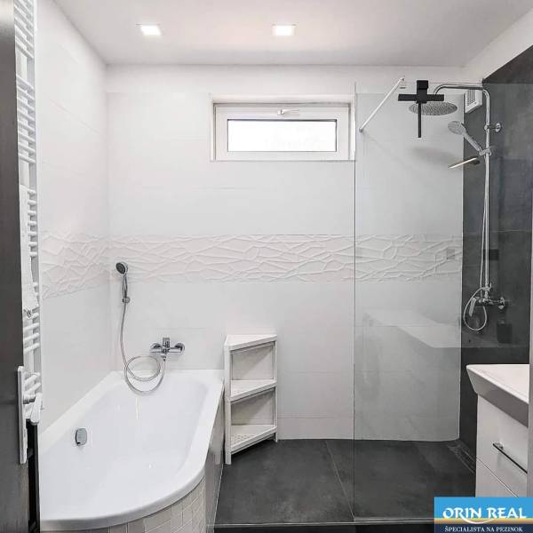 Bathroom in a 2-room apartment with a bathtub and shower, white tiles.