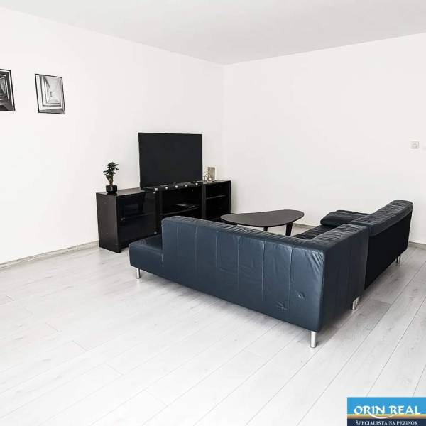 Living room in a two-room apartment with a wooden decor floor and a black sofa.
