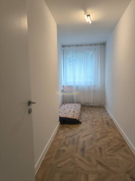 A narrow room with a light wall, a floor with a wooden decor, and a mattress. 4-room apartment.