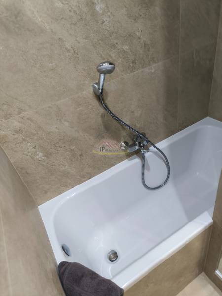 A bathroom in a 4-room apartment with a bathtub lined with light ceramic tiles.