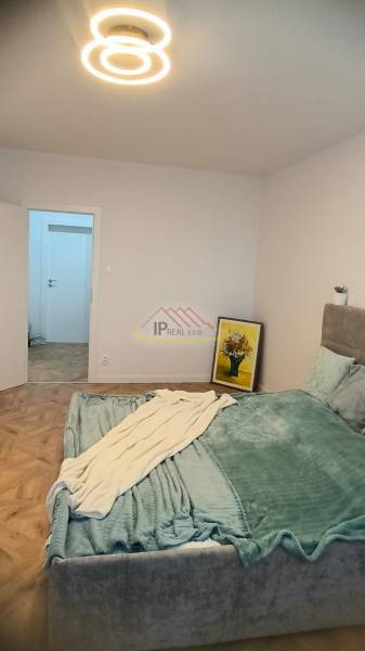 Bedroom in a 4-room apartment with a bed, wood-patterned flooring, and a modern chandelier.