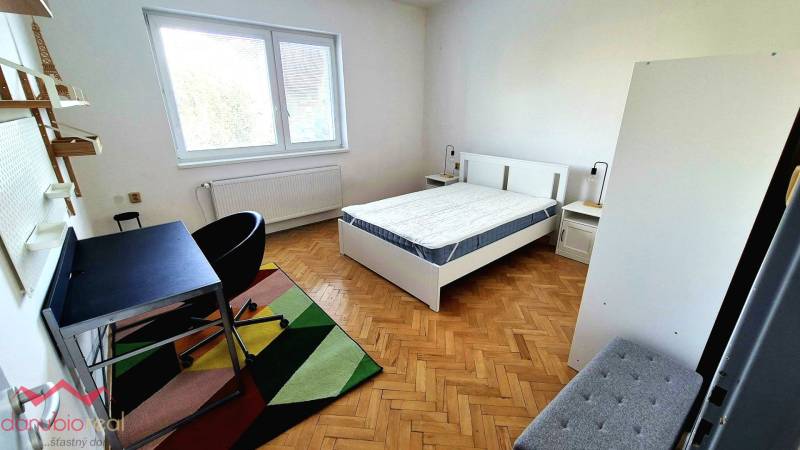 Bright bedroom in a three-room apartment with wood-patterned flooring and a writing desk.