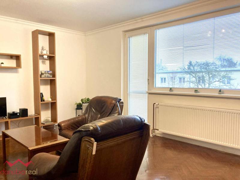 Living room in a three-room apartment with a wooden decor floor, large window, and leather armchairs.