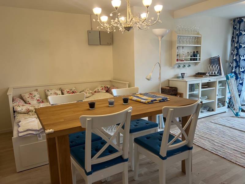 Dining area with a wooden table, white chairs, curtains, and a floor with a wooden decor in a cottage.