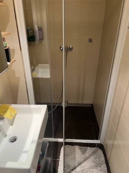 Shower corner and sink in the cottage bathroom, light tiles, dark floor.