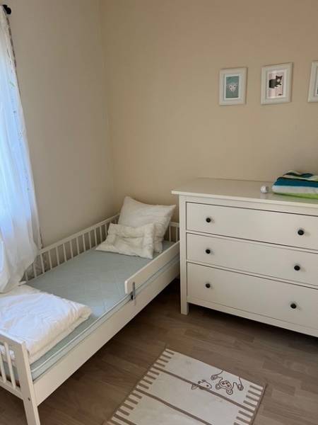A children's room in a cottage with a crib, a dresser, and a floor with a wooden decor.