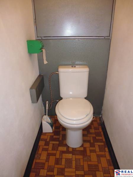 A toilet with a wooden decor floor in a studio apartment.