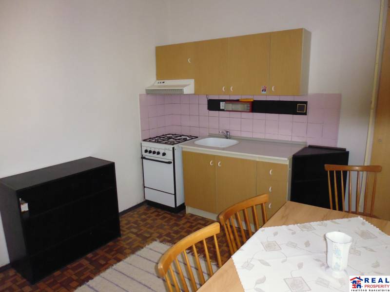 A kitchen in a studio apartment with a wooden decor floor and a dining table.