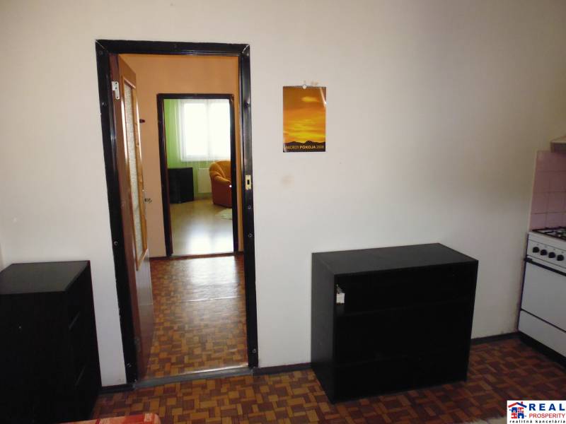 Room in a one-room apartment with a wooden decor floor, tiled stove, and furniture.