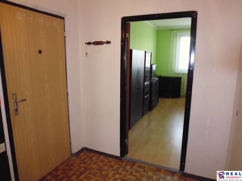 A hallway in a one-room apartment with a wooden decor floor and a green room.