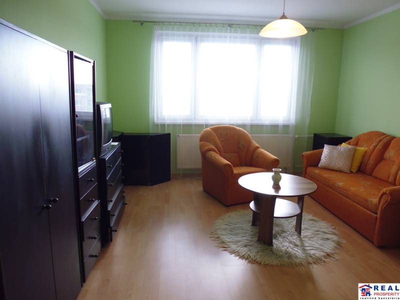 Living area in a studio apartment with wood-patterned flooring and orange seating.