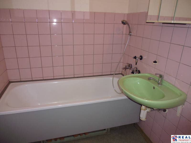 Bathroom with a bathtub, green sink, and pink tiles in a studio apartment.