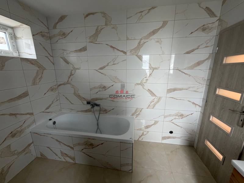 A bathroom with a bathtub and marble-patterned tiles in a family house.