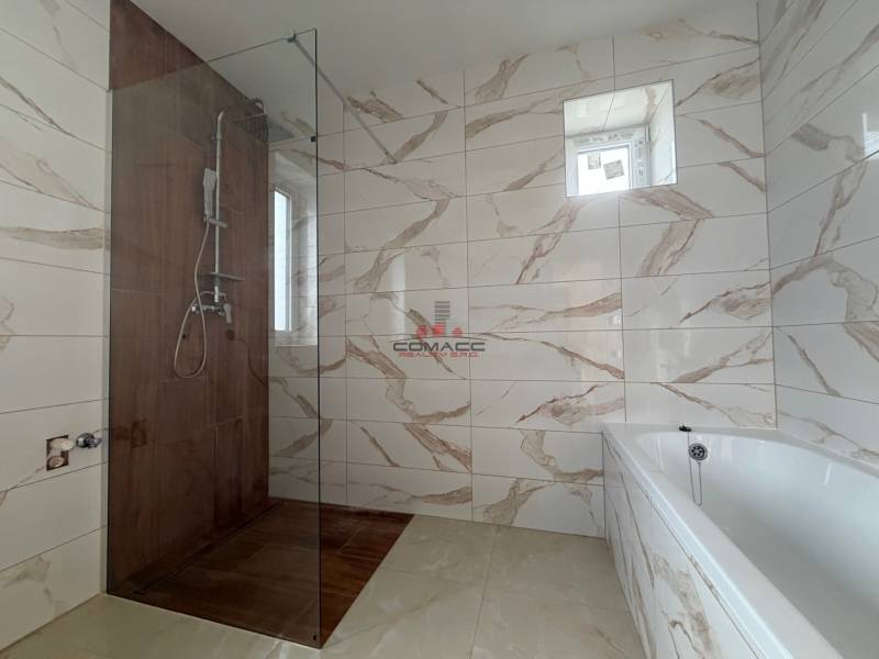 Bathroom in a family house with marble-patterned tiles and a shower enclosure.